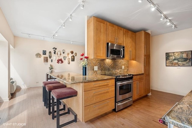 kitchen featuring stainless steel appliances, tasteful backsplash, rail lighting, light wood-type flooring, and a kitchen bar