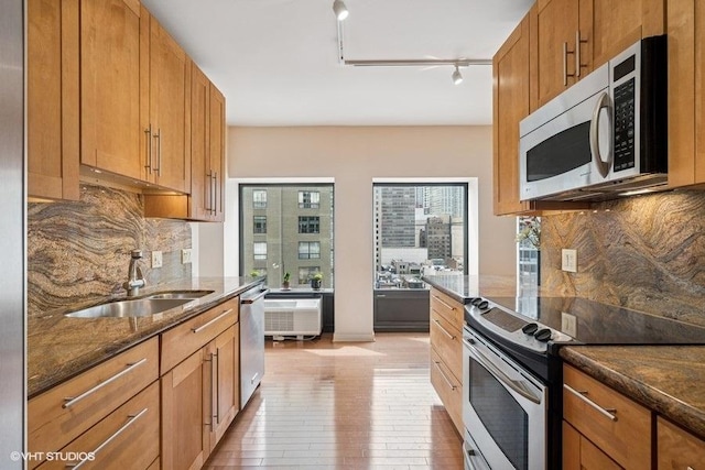 kitchen featuring light wood-style flooring, a sink, track lighting, dark stone counters, and appliances with stainless steel finishes