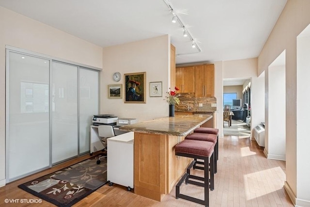 kitchen with a peninsula, a breakfast bar, stone countertops, track lighting, and light wood-type flooring