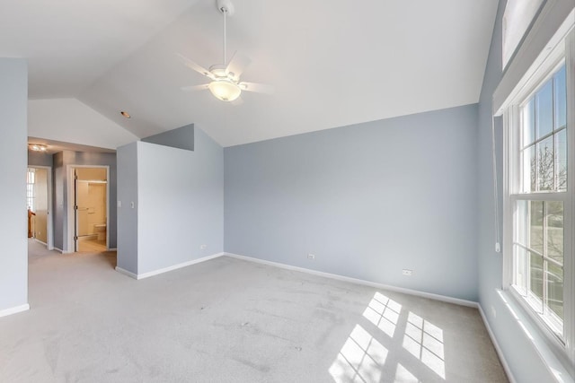spare room with vaulted ceiling, light colored carpet, baseboards, and a ceiling fan
