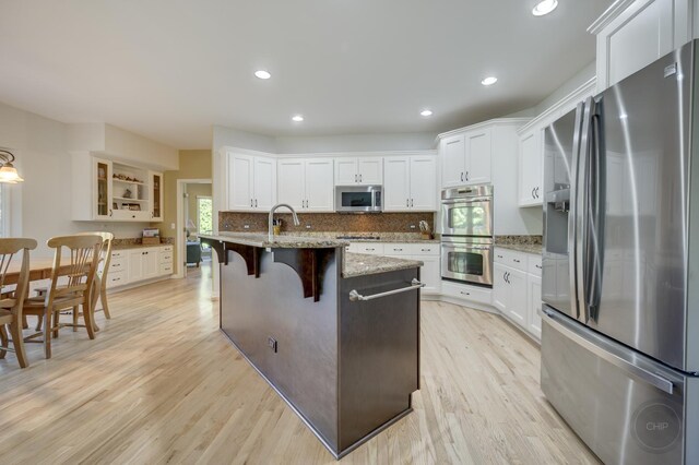 2411 Williamstown Ct, Naperville, IL 60564 - kitchen with stainless steel appliances, light wood finished floors, white cabinets, a kitchen island with sink, and a breakfast bar area