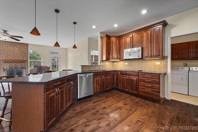 kitchen with stainless steel appliances, washing machine and dryer, a kitchen breakfast bar, a sink, and dark wood-type flooring