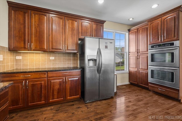 kitchen featuring appliances with stainless steel finishes, dark wood-style flooring, dark stone countertops, decorative backsplash, and recessed lighting
