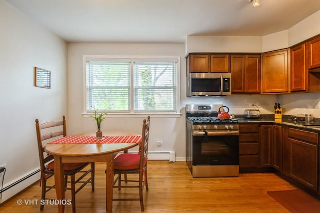 kitchen with appliances with stainless steel finishes, a baseboard radiator, dark countertops, and light wood-style flooring