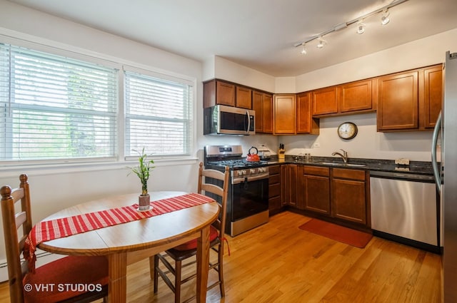 kitchen with appliances with stainless steel finishes, a sink, light wood-style flooring, brown cabinetry, and rail lighting