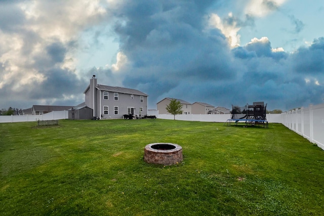 view of yard with a trampoline, a fire pit, and a fenced backyard