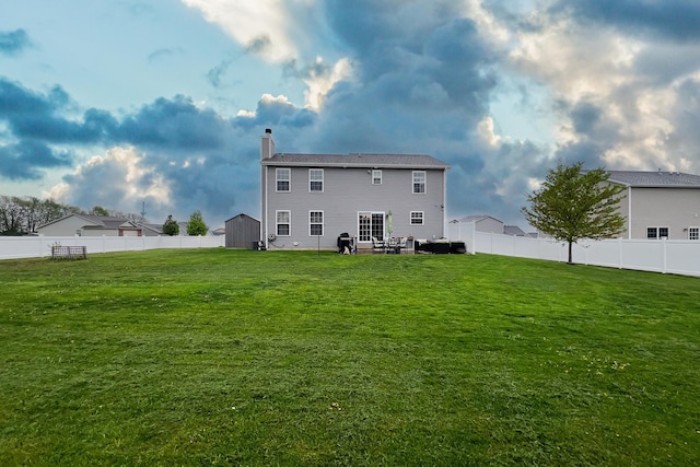 back of property featuring a chimney, a yard, an outbuilding, a fenced backyard, and a storage unit