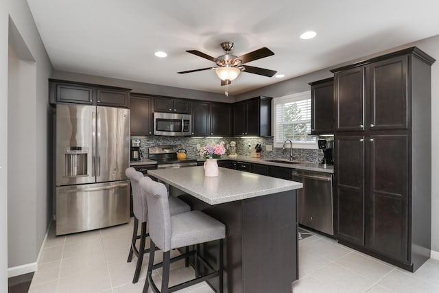 kitchen featuring ceiling fan, a sink, a kitchen bar, backsplash, and appliances with stainless steel finishes