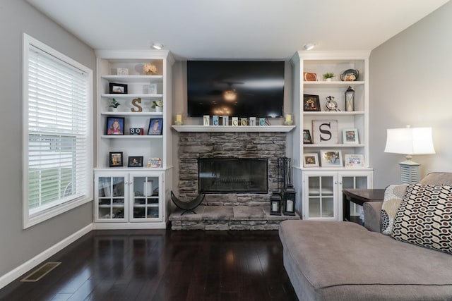 living room featuring baseboards, a stone fireplace, visible vents, built in shelves, and wood finished floors