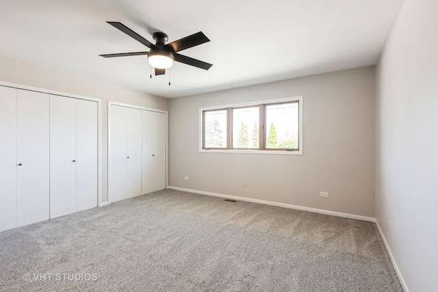 unfurnished bedroom featuring multiple closets, carpet floors, baseboards, and ceiling fan