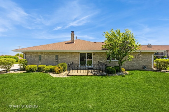 back of property with brick siding, a chimney, and a yard