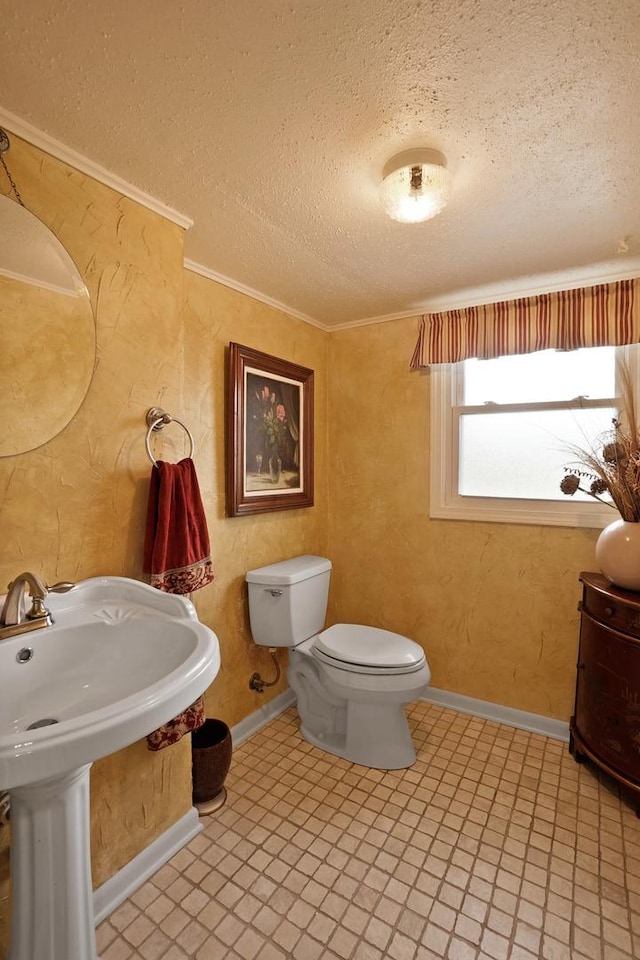 bathroom featuring a textured ceiling, crown molding, toilet, and baseboards