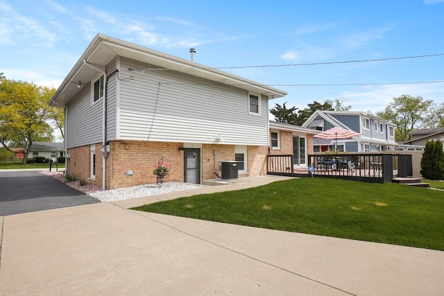 back of property with central air condition unit, brick siding, a yard, and a deck