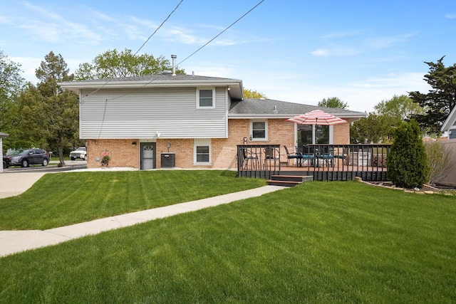 rear view of property featuring a lawn, brick siding, a wooden deck, and roof with shingles