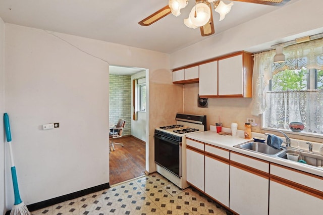 kitchen featuring a sink, white gas range, white cabinets, ceiling fan, and light countertops