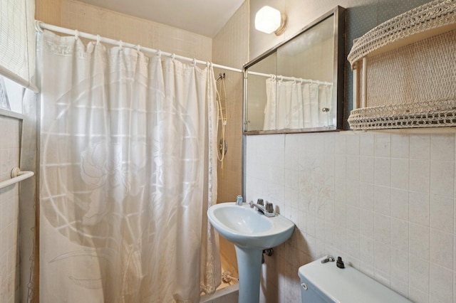 bathroom with a sink, curtained shower, tile walls, and toilet