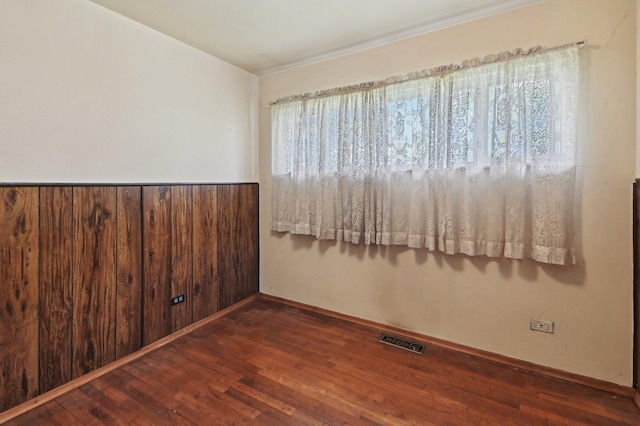 empty room featuring a wainscoted wall, wood walls, visible vents, baseboards, and hardwood / wood-style flooring