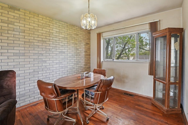 dining area featuring a notable chandelier, visible vents, brick wall, and wood-type flooring