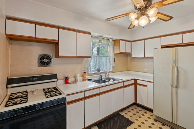 kitchen with freestanding refrigerator, range with gas stovetop, ceiling fan, a sink, and white cabinetry