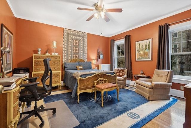 bedroom with a ceiling fan, multiple windows, ornamental molding, and wood finished floors