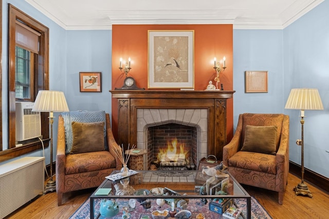 sitting room featuring radiator, ornamental molding, cooling unit, a tiled fireplace, and wood finished floors