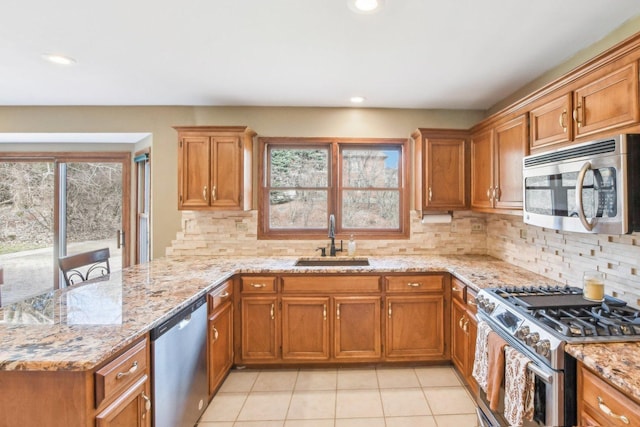 kitchen featuring light tile patterned floors, stainless steel appliances, brown cabinetry, and a sink