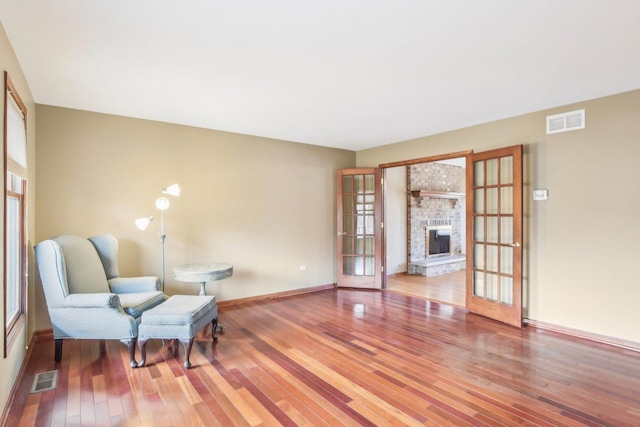 living area featuring baseboards, hardwood / wood-style floors, visible vents, and a brick fireplace