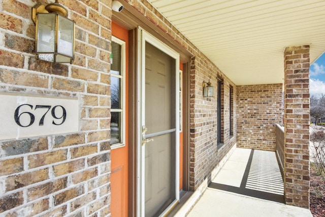 doorway to property with a porch and brick siding