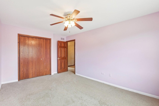 unfurnished bedroom featuring light colored carpet, a closet, baseboards, and a ceiling fan