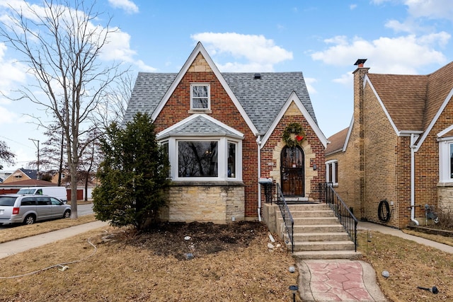 english style home with brick siding, roof with shingles, and a chimney