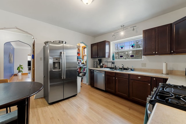 kitchen with dark brown cabinets, a sink, light wood-type flooring, light countertops, and appliances with stainless steel finishes
