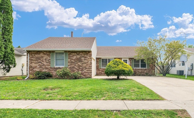 ranch-style home featuring driveway, brick siding, central AC unit, roof with shingles, and a front lawn
