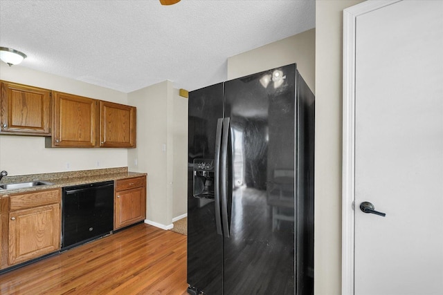 kitchen featuring brown cabinets, light wood-style flooring, a sink, a textured ceiling, and black appliances