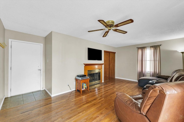living area featuring a fireplace with flush hearth, baseboards, a ceiling fan, and wood finished floors