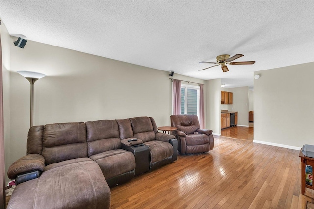 living area with baseboards, light wood-style flooring, ceiling fan, and a textured ceiling