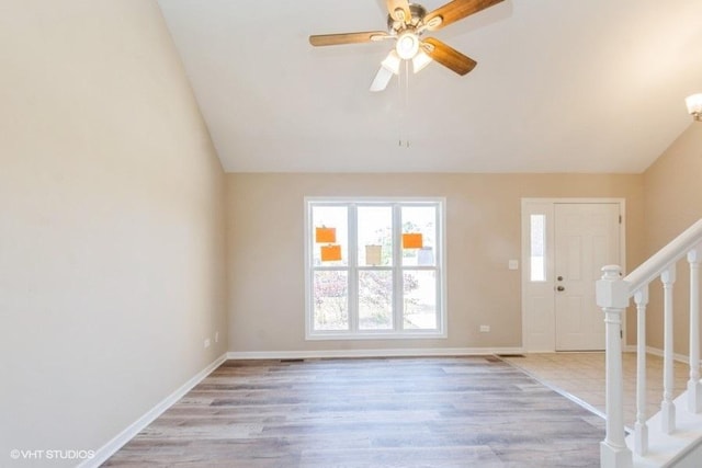 foyer entrance featuring vaulted ceiling, light wood finished floors, ceiling fan, stairway, and baseboards