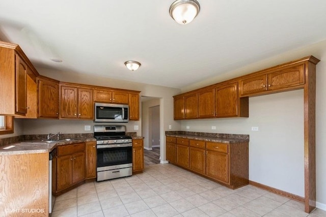 kitchen with a sink, brown cabinets, baseboards, dark countertops, and appliances with stainless steel finishes