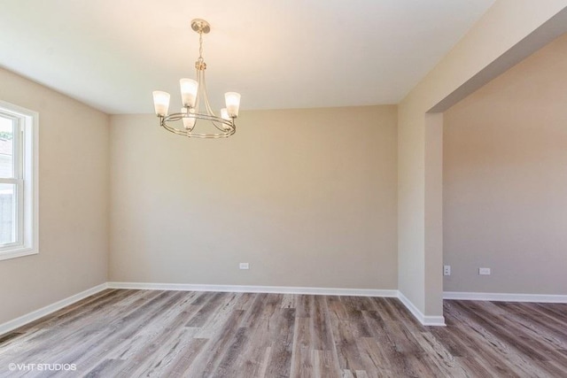 spare room featuring a chandelier, baseboards, and wood finished floors