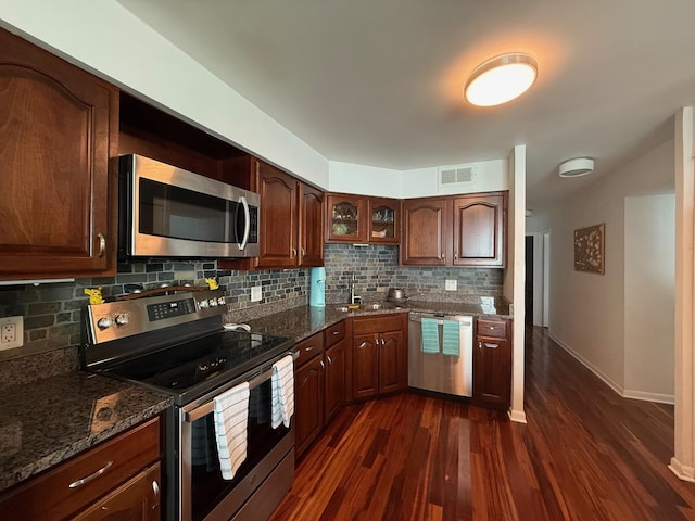 kitchen with dark stone counters, appliances with stainless steel finishes, tasteful backsplash, and dark wood-style floors