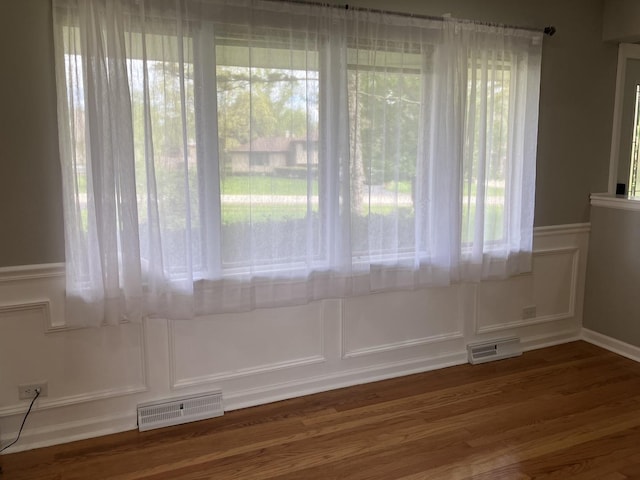 unfurnished dining area with wainscoting, a decorative wall, visible vents, and wood finished floors