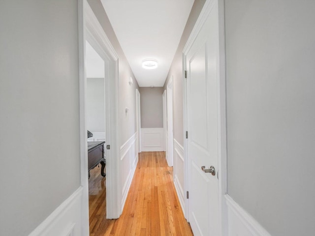 corridor with light wood-style flooring, a decorative wall, and a wainscoted wall