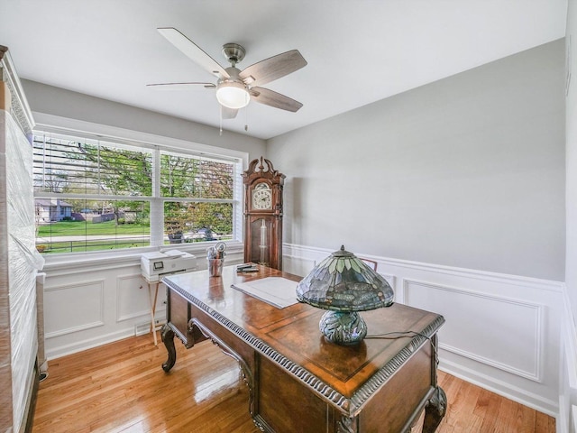 office area featuring ceiling fan, light wood-style flooring, a decorative wall, and a wainscoted wall