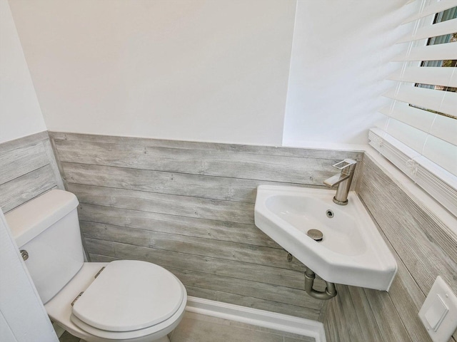bathroom featuring a wainscoted wall, toilet, tile walls, and a sink