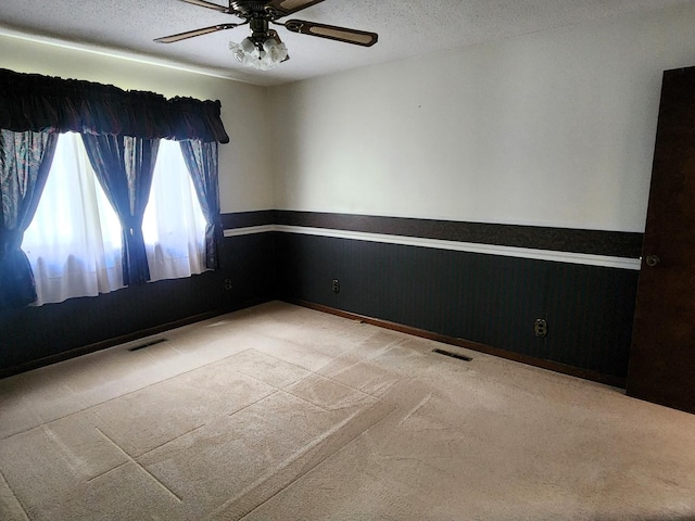 carpeted spare room featuring wainscoting, ceiling fan, and a textured ceiling
