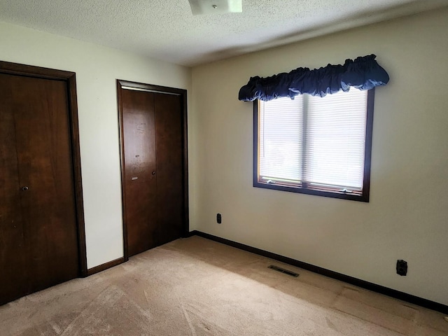 unfurnished bedroom with light carpet, a textured ceiling, and baseboards