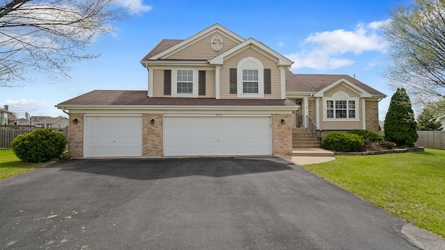 tri-level home featuring brick siding, fence, a shingled roof, a front yard, and aphalt driveway