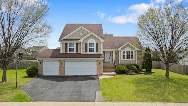 tri-level home with brick siding, driveway, fence, and a front yard