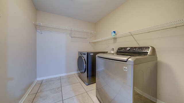 laundry area featuring washing machine and clothes dryer, laundry area, light tile patterned flooring, and baseboards