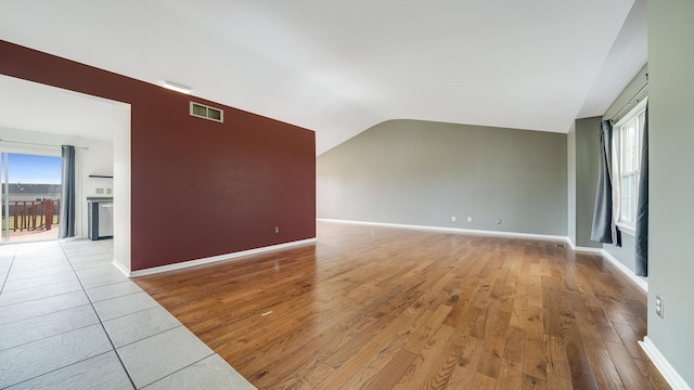 unfurnished living room featuring vaulted ceiling, light wood-style flooring, baseboards, and visible vents