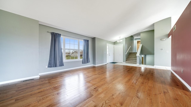 unfurnished living room with wood-type flooring, visible vents, lofted ceiling, and stairway